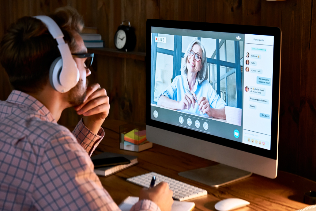 Man wearing headphones with hand on chin while observing woman speaking on monitor screen.