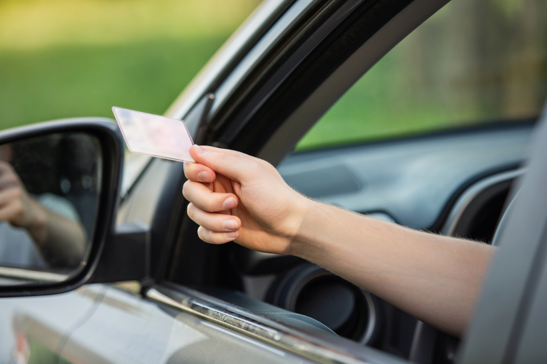 Person sitting on car and hanging license out of window.