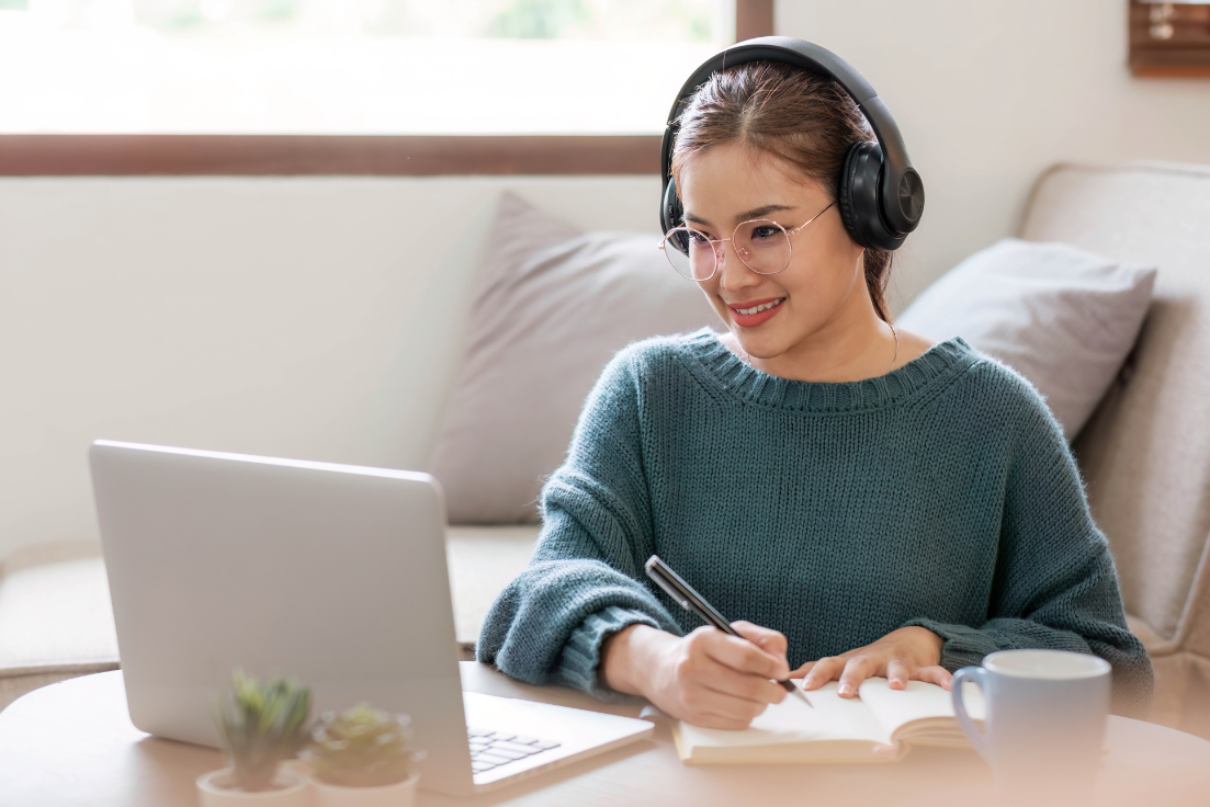 Woman studying with headphones and looking at laptop.