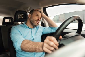Man driving with onr hands and with stressed expression.