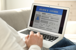A person using a laptop to fill out an online driver's license registration form. The screen displays a blue header with the words 