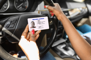 Woman holding license next to steering wheel.