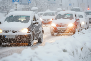 Cars navigating a snow-covered road during heavy snowfall, with headlights illuminating the wintry scene.