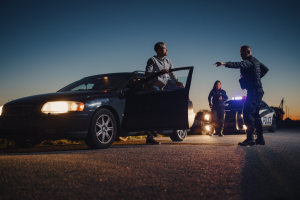 A police officer is writing a ticket while standing beside a stopped car. The officer is holding a citation in their hands, with their back partially facing the camera. The car they are addressing is parked by the roadside.