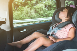 A young child peacefully asleep in a car seat, safely buckled in the backseat of a moving vehicle.