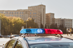 The top of a police vehicle with blue and red lights, parked in front of government buildings, indicating law enforcement presence.