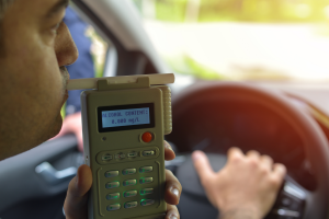 A man taking a breathalyzer test behind the wheel, with the device displaying an alcohol content of 0.000 mg/L.