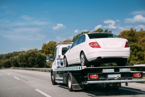 A white sedan being transported on the back of a flatbed tow truck on a highway.