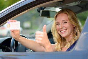 Woman holding license and thumbs up while sitting on car.