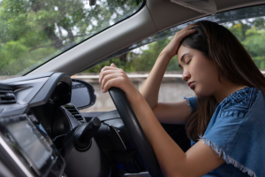 Woman with hand on forehand while sitting on car drivers seat.