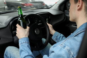 A person driving a car while holding a green bottle of beer.