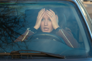 A person inside a car with hands on their head, looking stressed through the windshield.