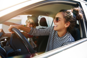 Two women sitting in a car, smiling and enjoying the moment; the driver has her hands on the steering wheel.