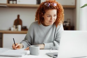 Woman observing her laptop and taking notes.