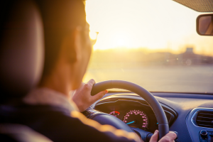 View from the back of a mans head. He is driving a car and there is a sunset on the background.