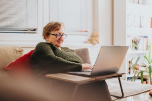 An elderly woman engaging with her laptop in a cozy living room.