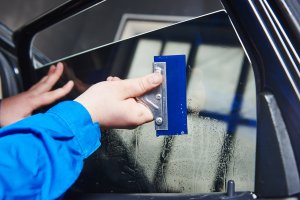 Automobile mechanic technician applying foil on window in repair garage workshop.