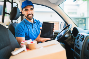 Man sitting on car showing tablet. Cardboard boxes next to him.